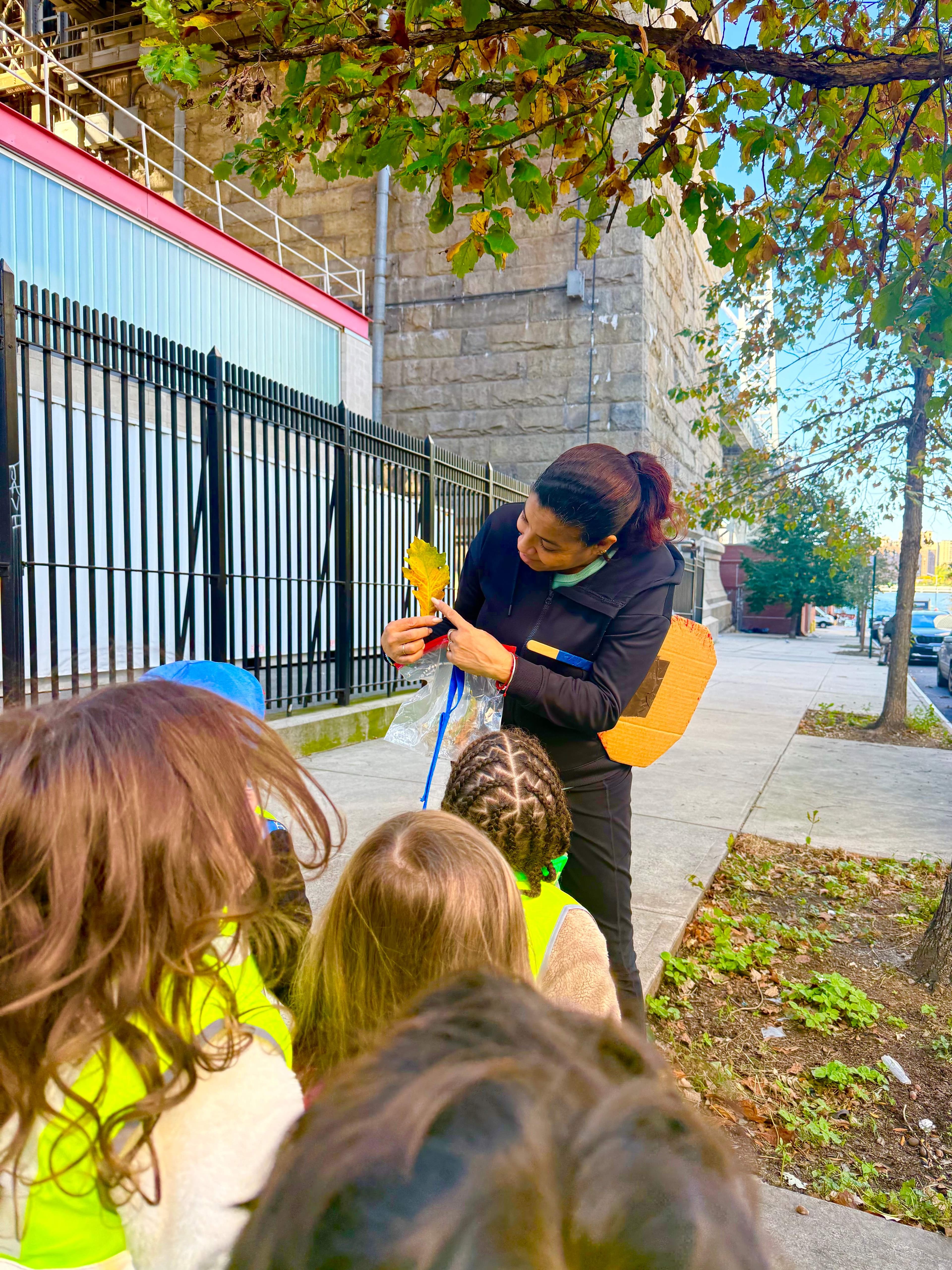 Children examining a colorful leaf with their teacher outdoors